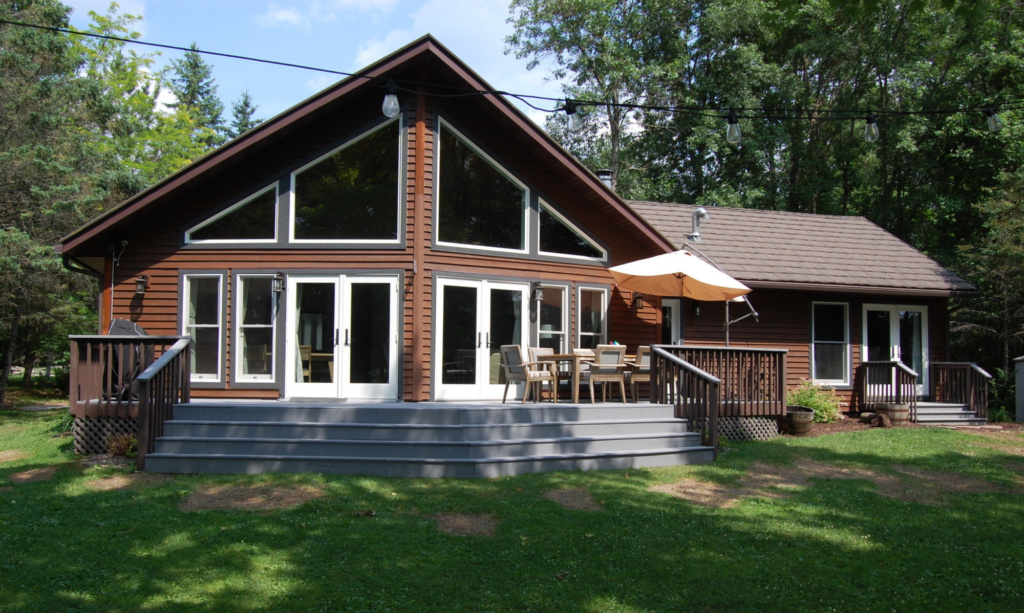 A front view of Bone Lake Escape, looking on the deck with seating for 8, a large, cantilever umbella, and propane grill.