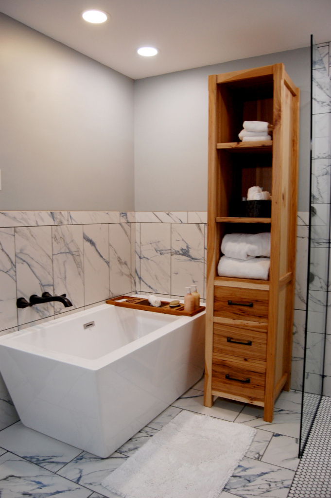 Soaker bath tub surrounded by marble tile; a bath caddy rests across the tub with complementary toiletries.